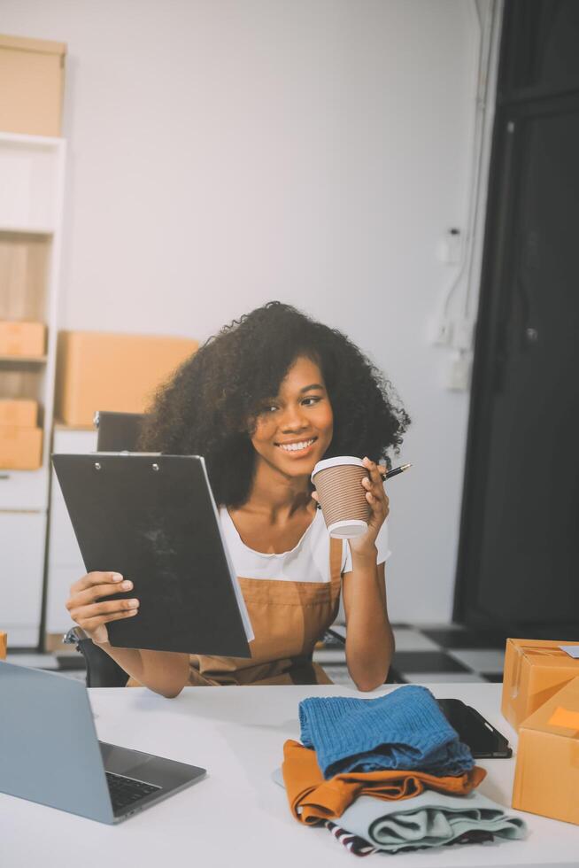 Startup SME small business entrepreneur of freelance Asian woman wearing apron using laptop and box to receive and review orders online to prepare to pack sell to customers, online sme business ideas. photo