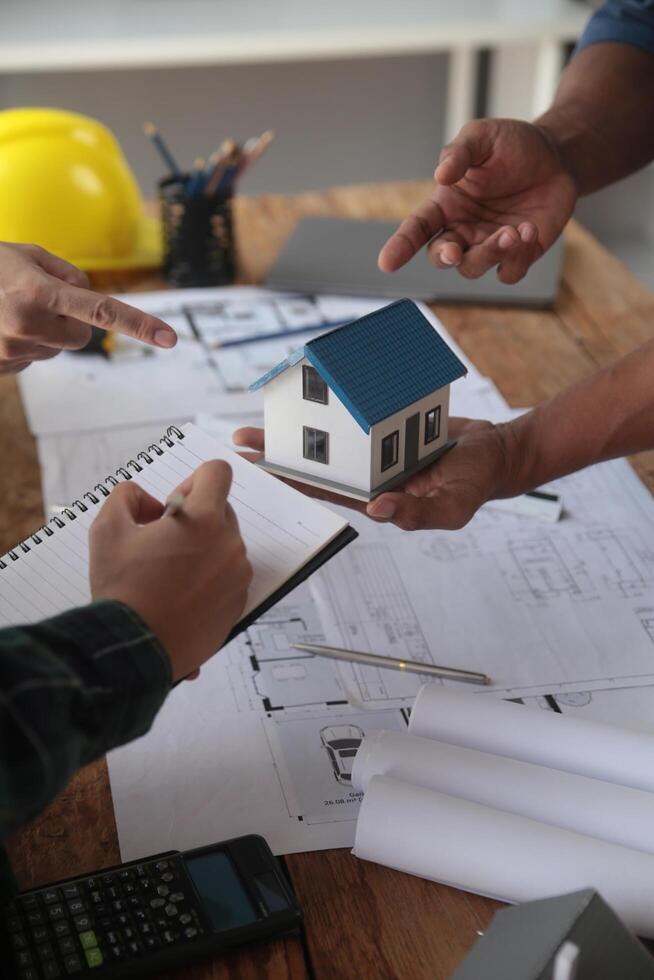 ingenieros son consultante el equipo a diseño un arquitectónico estructura para clientela con planos y edificio modelos a trabajo a oficina. foto