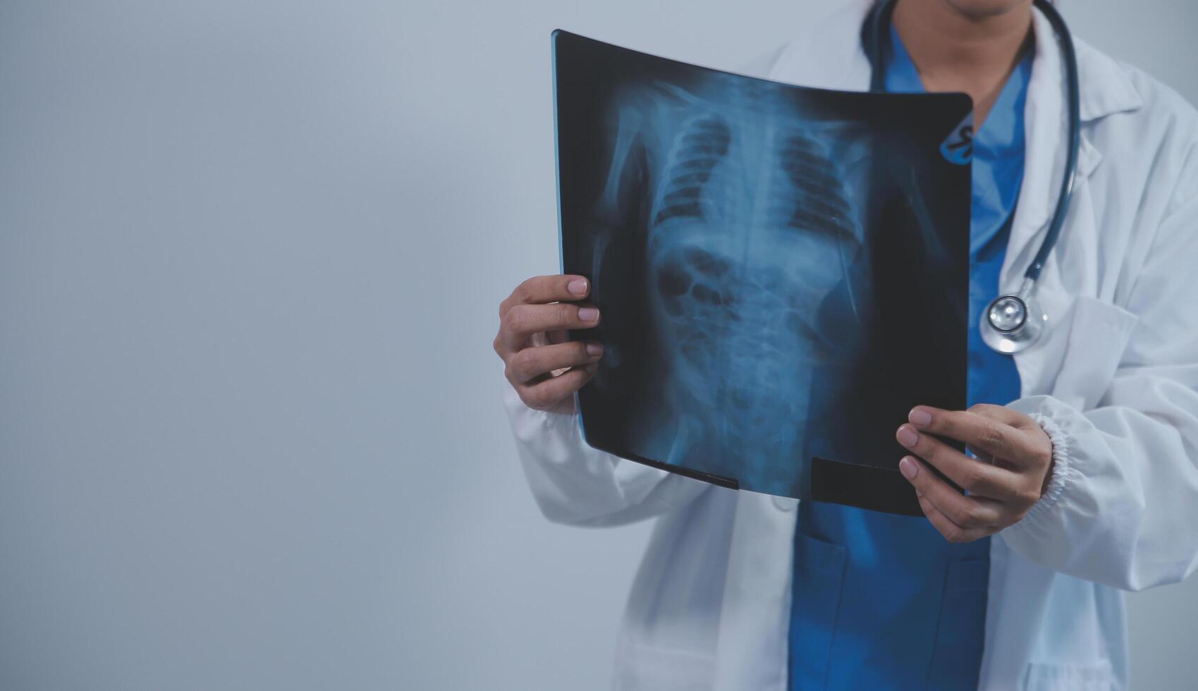 Asian Muslim doctor in hijab and scrubs headphones around her neck Stand confidently in the medical office, isolated on white background, holding x-ray film. photo