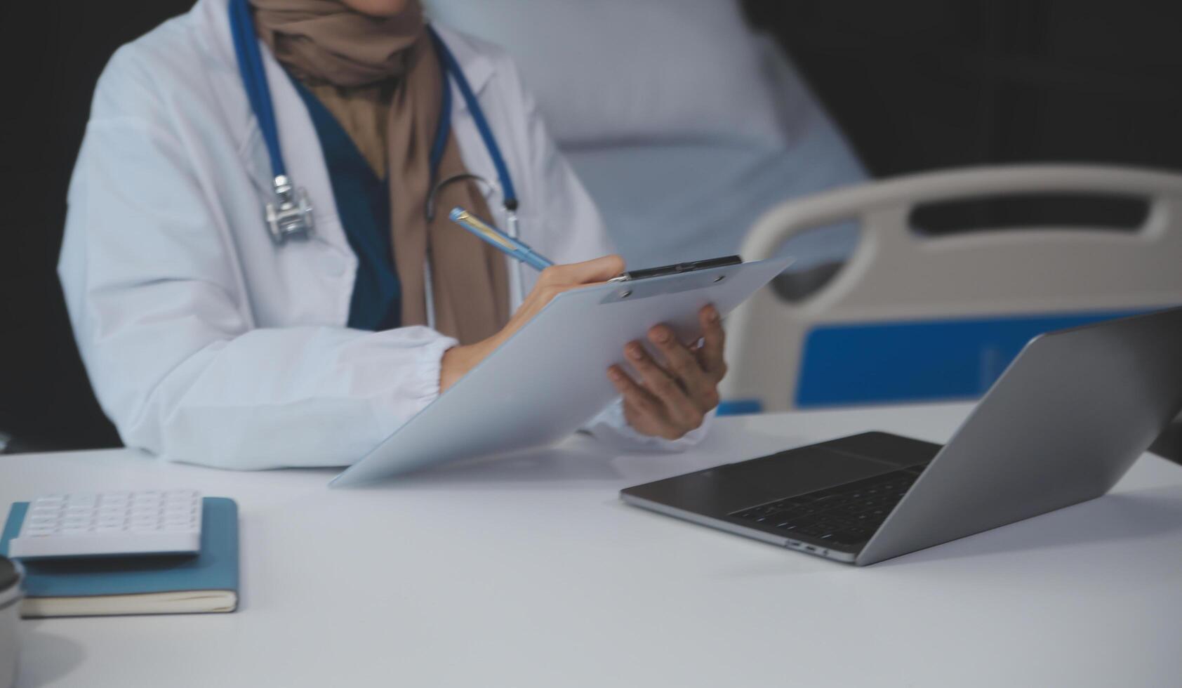 A professional and focused Asian female doctor in scrubs is working and reading medical research on her laptop in her office at a hospital. photo