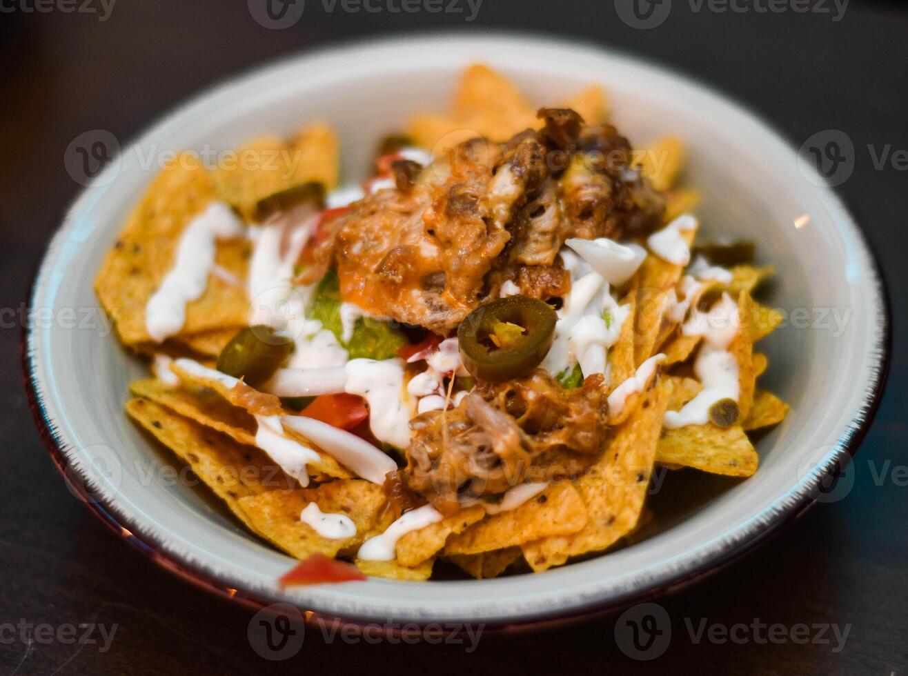 Serving of nachos with meat, cheese, white sauce and jalapenos photo