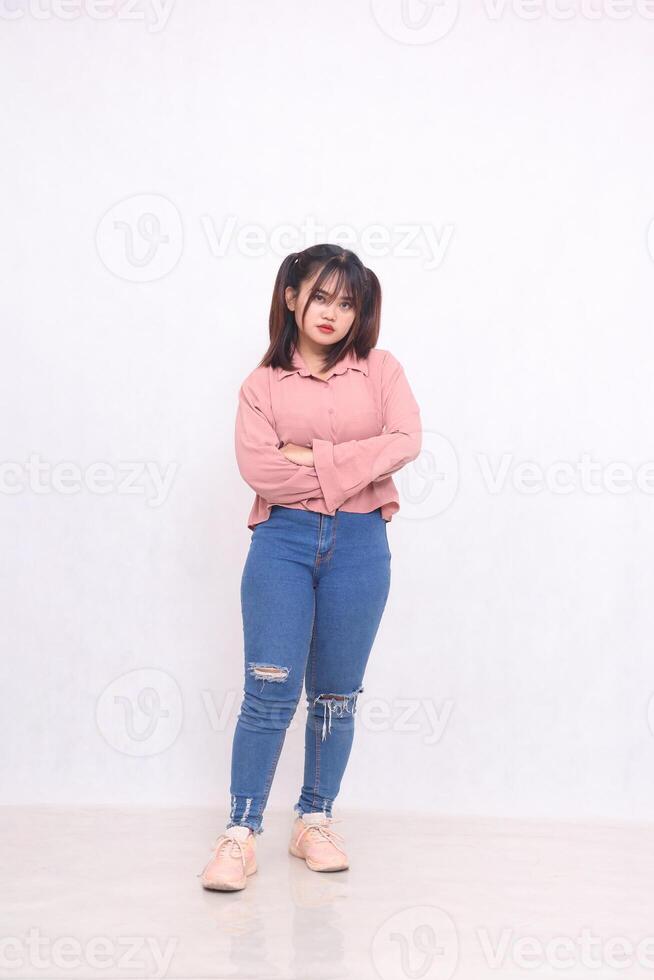 Smiling cheerful beautiful black-haired woman in her 20s wearing a basic pink shirt standing working style with her arms crossed studio portrait on white background for service promotion full body photo