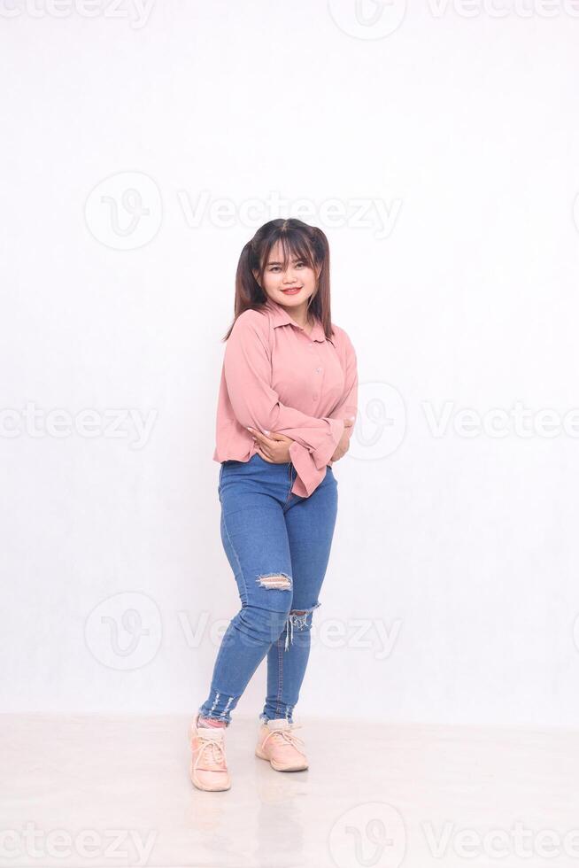 Smiling cheerful beautiful black-haired woman in her 20s wearing a basic pink shirt standing working style while smiling with arms casual studio portrait on white background for service promotion photo