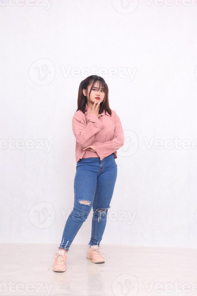 Smiling cheerful black-haired beautiful woman in her 20s wearing basic pink shirt standing working style with arms and chin studio portrait white background for services promotion photo