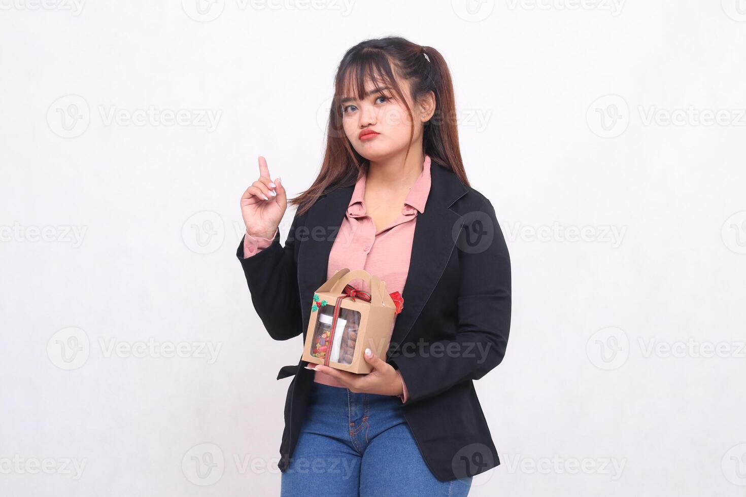 Beautiful Asian girl in her 20s pouting excitedly pointing up Christmas gift in the form of hamper in hand on white background for advertising materials, banners, billboards photo