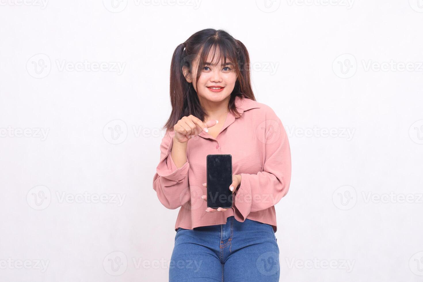 Beautiful happy asian indonesia woman in her 20s wearing casual shirt holding cellphone green screen pointing gadget on white background studio portrait for banner ad, banner, billboard photo