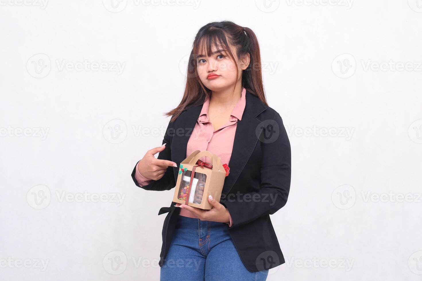 Beautiful Asian girl in her 20s pouting excitedly pointing to a Christmas gift in the form of a hamper in her hand on a white background for advertising materials, banners, billboards photo