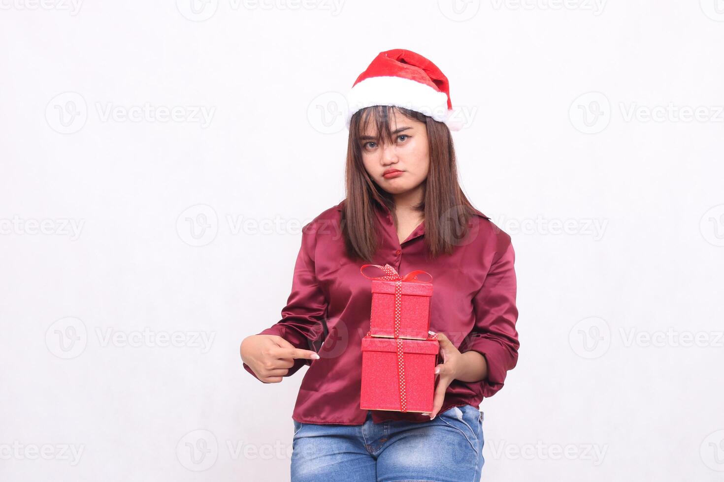 beautiful young asian indonesian girl pouting carrying gift box in christmas santa claus hat modern red shirt outfit pointed side box on white background for promotion and advertising photo