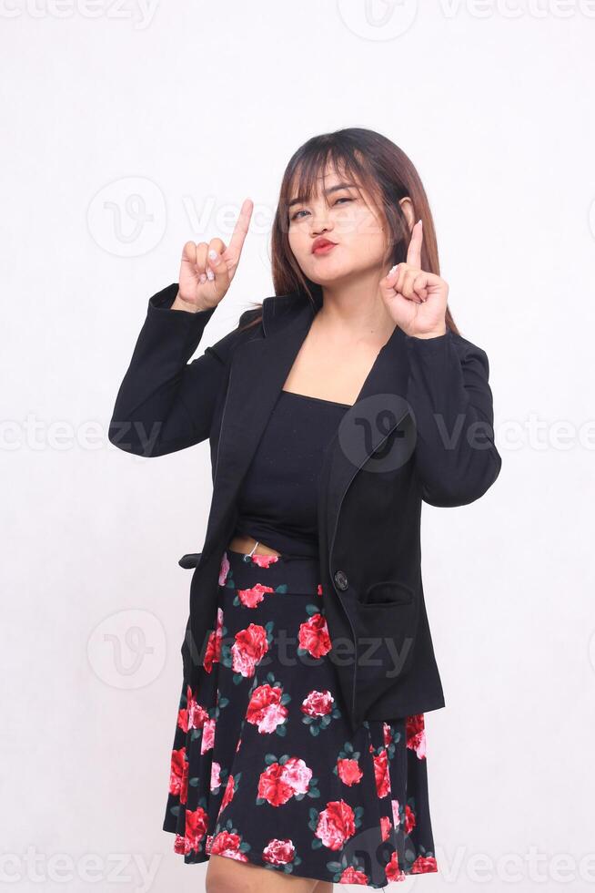 Beautiful Asian Indonesian girl in a casual professional office skirt, cheerful, right hand pointing upwards on a white background for promotion, advertising, banner photo