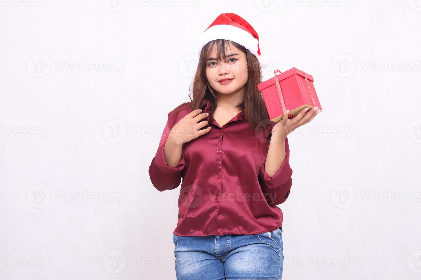 retrato de un hermosa joven asiático niña que lleva un regalo caja a Navidad Papa Noel claus sombrero moderno brillante rojo camisa atuendo izquierda mano levantamiento caja en blanco antecedentes para promoción y publicidad foto
