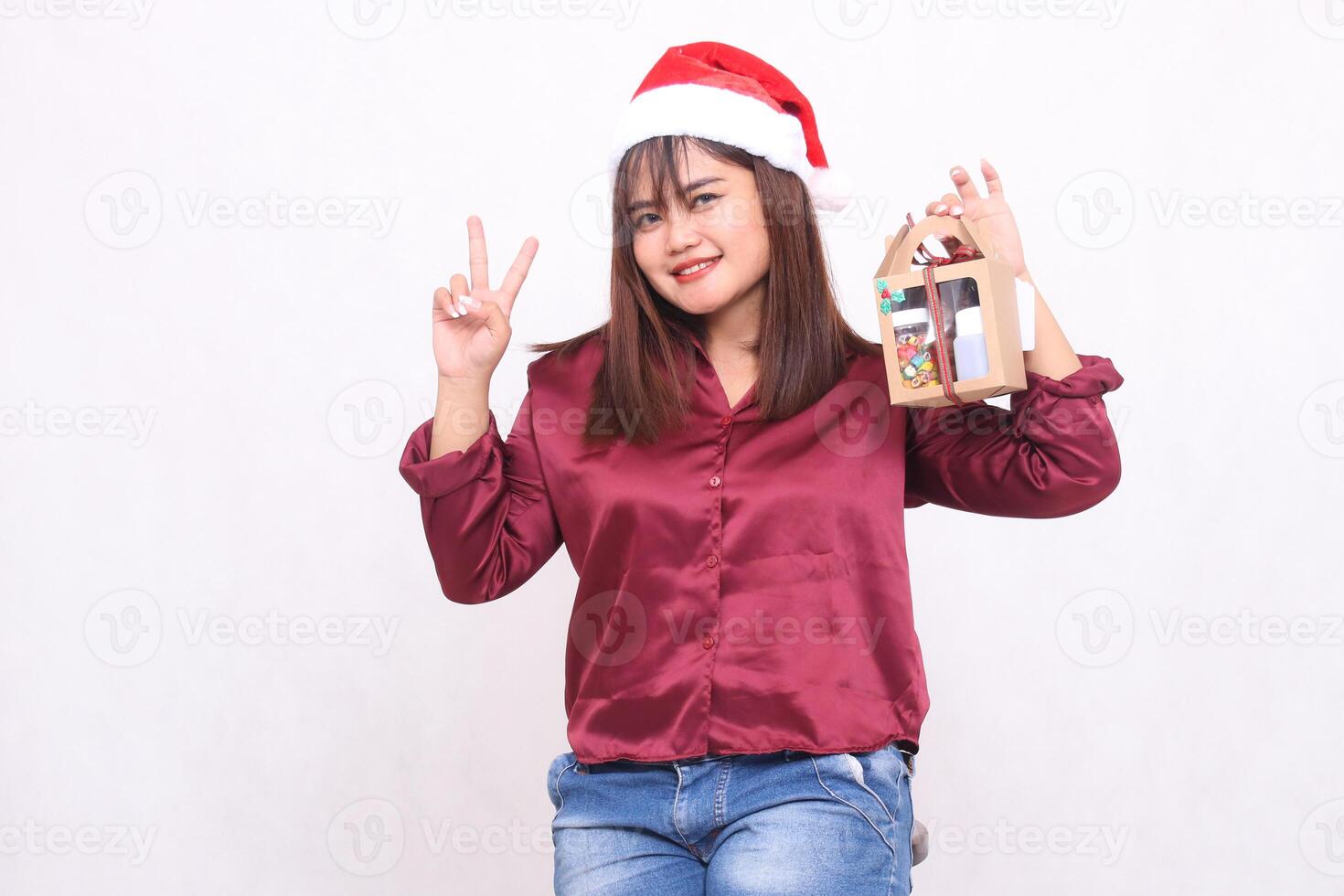 beautiful young woman southeast asian smile hand sign number 2 bringing gift hamper in christmas wear santa claus hat modern red shirt outfit white background for promotion and advertising photo