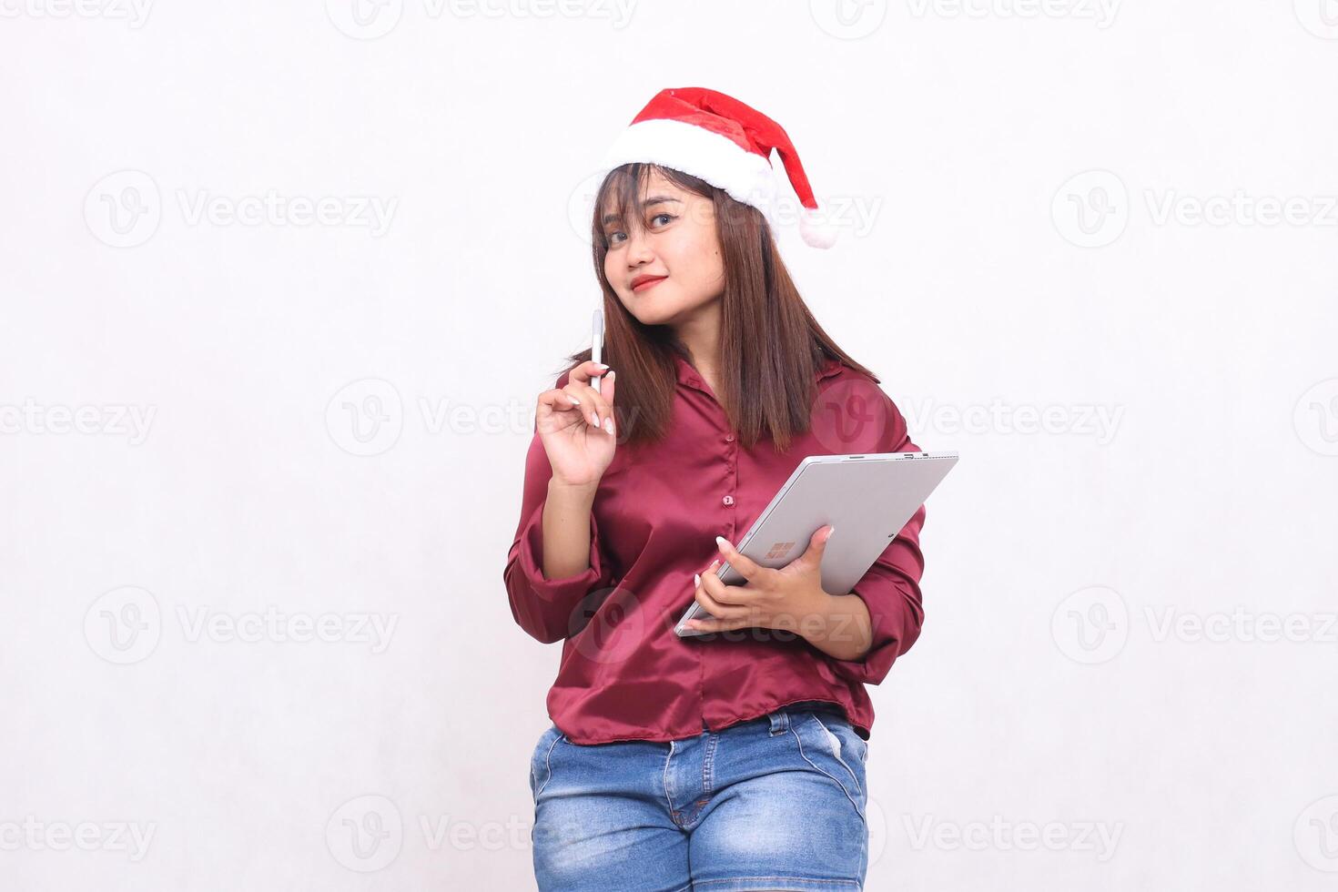 hermosa joven Sureste asiático mujer sonriente pensando mirando adelante mientras que lleva ordenador portátil tableta a Navidad vistiendo Papa Noel sombrero vistiendo rojo camisa moderno blanco antecedentes para promoción y publicidad foto