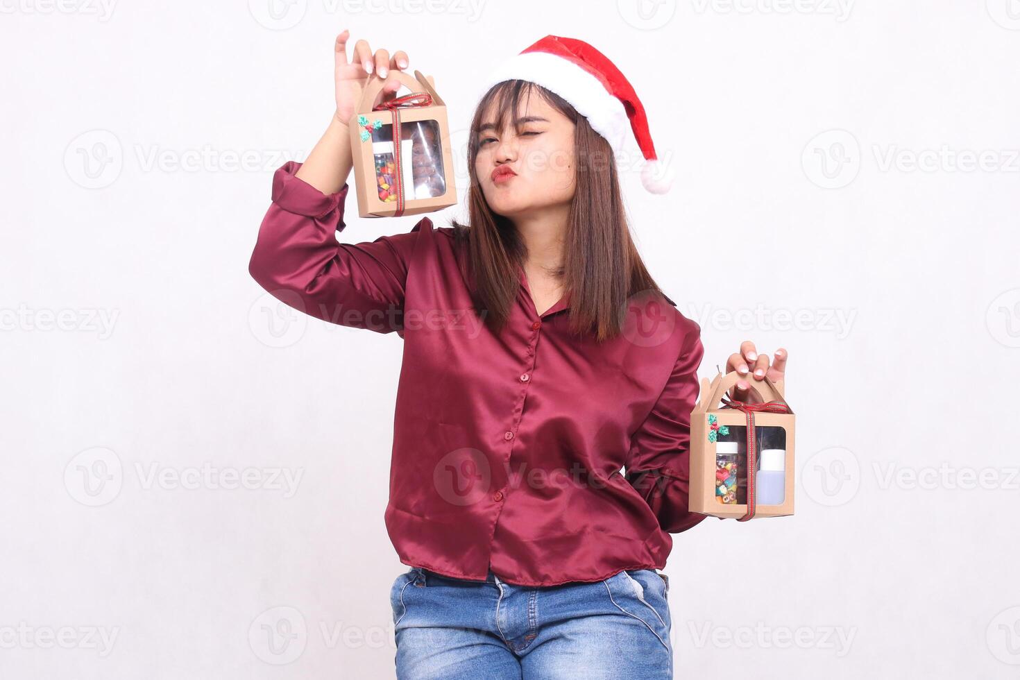 Beautiful young Southeast Asian woman kissing gifts carrying 2 boxes of gift hampers at Christmas wearing Santa Claus hat modern red shirt outfit white background for promotion and advertising photo