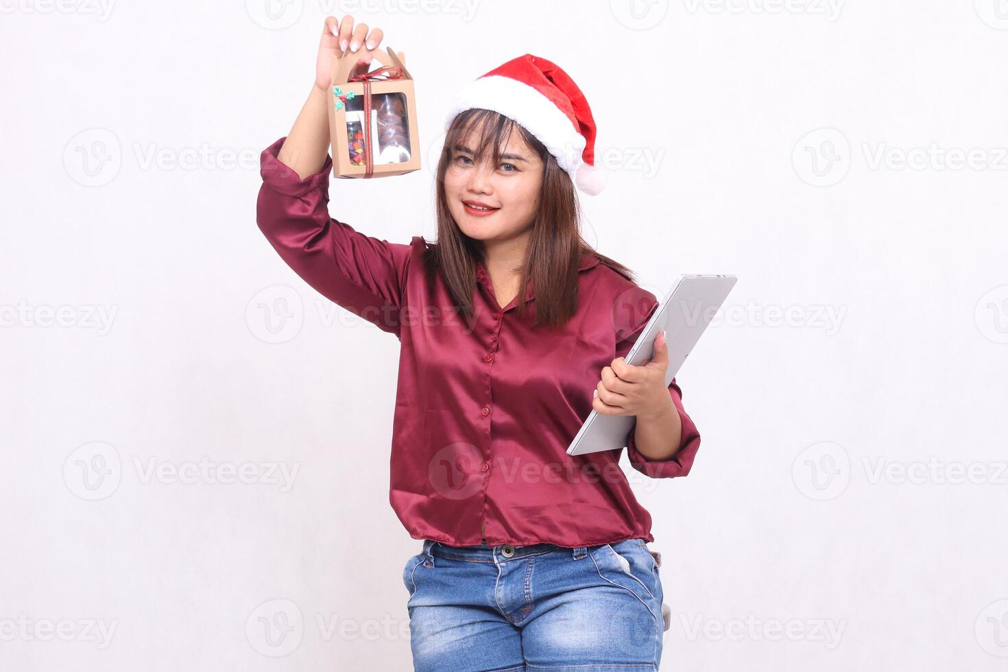 beautiful young woman southeast asia smile lift food package gift in hamper and laptop tablet in christmas wear santa hat modern red shirt outfit white background for promotion and advertising photo