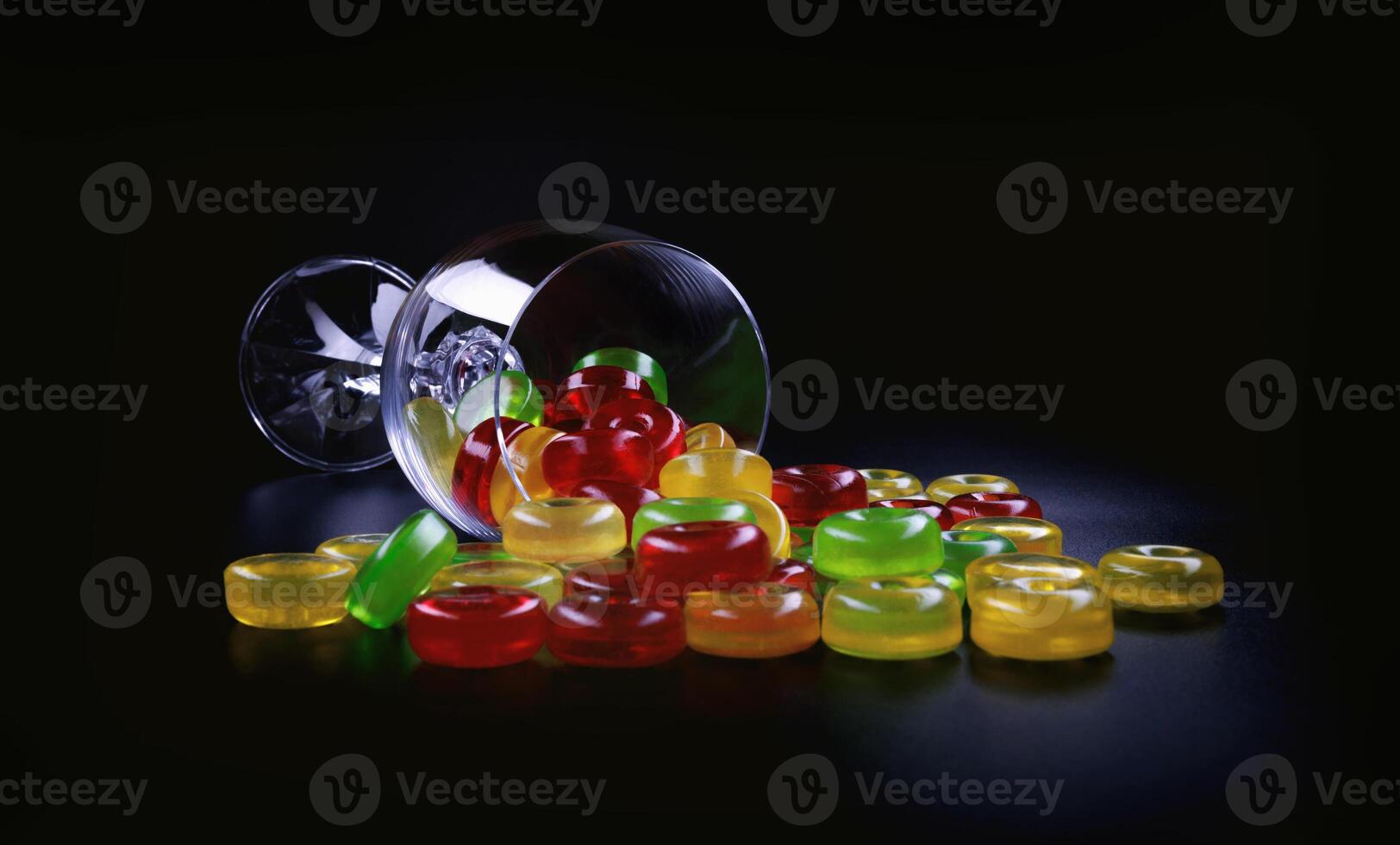 A lot of lollipops are scattered from an overturned glass goblet. Multi-colored candies in a glass. photo