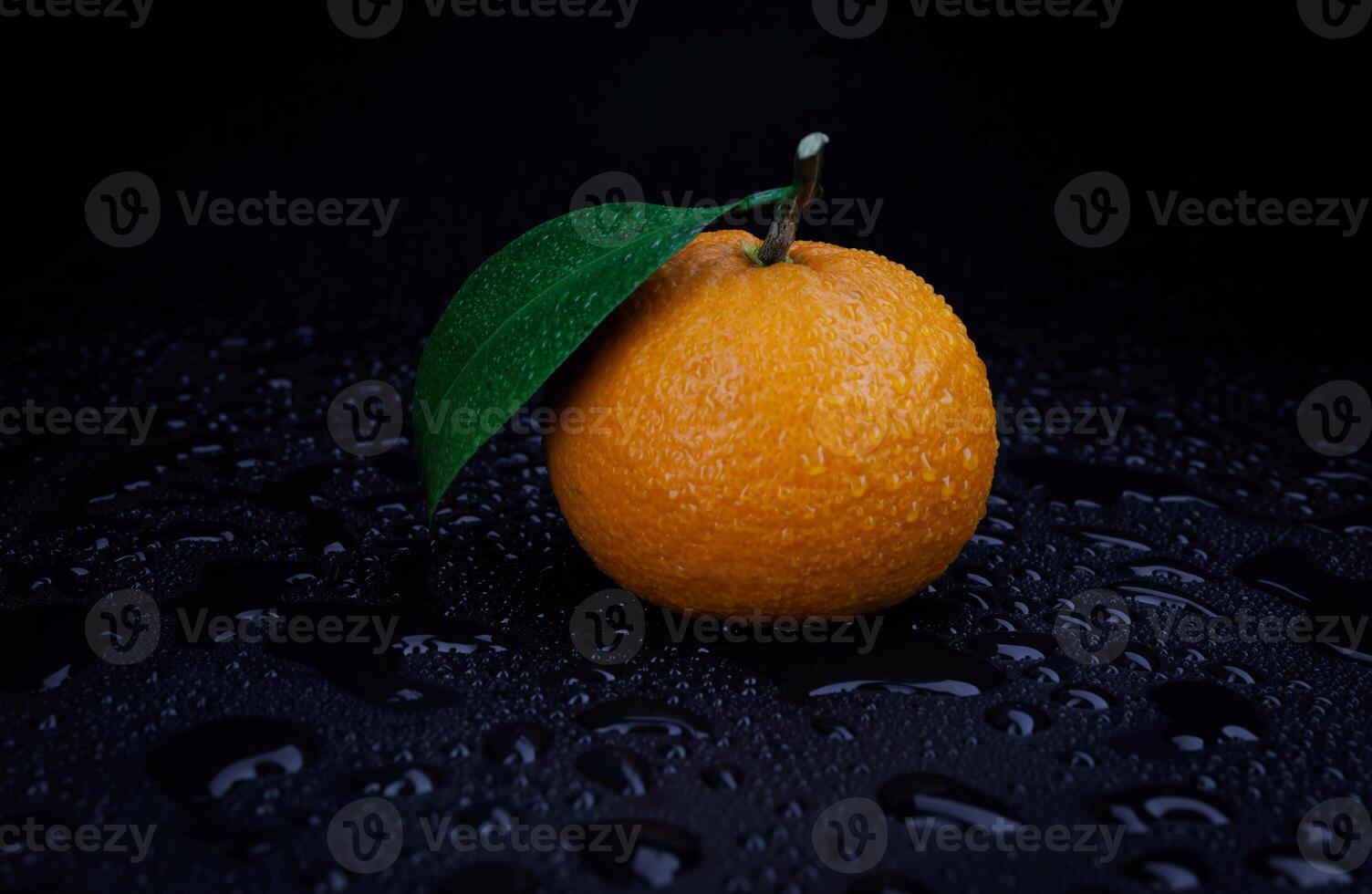 Ripe juicy tangerine on a black background with water drops. photo