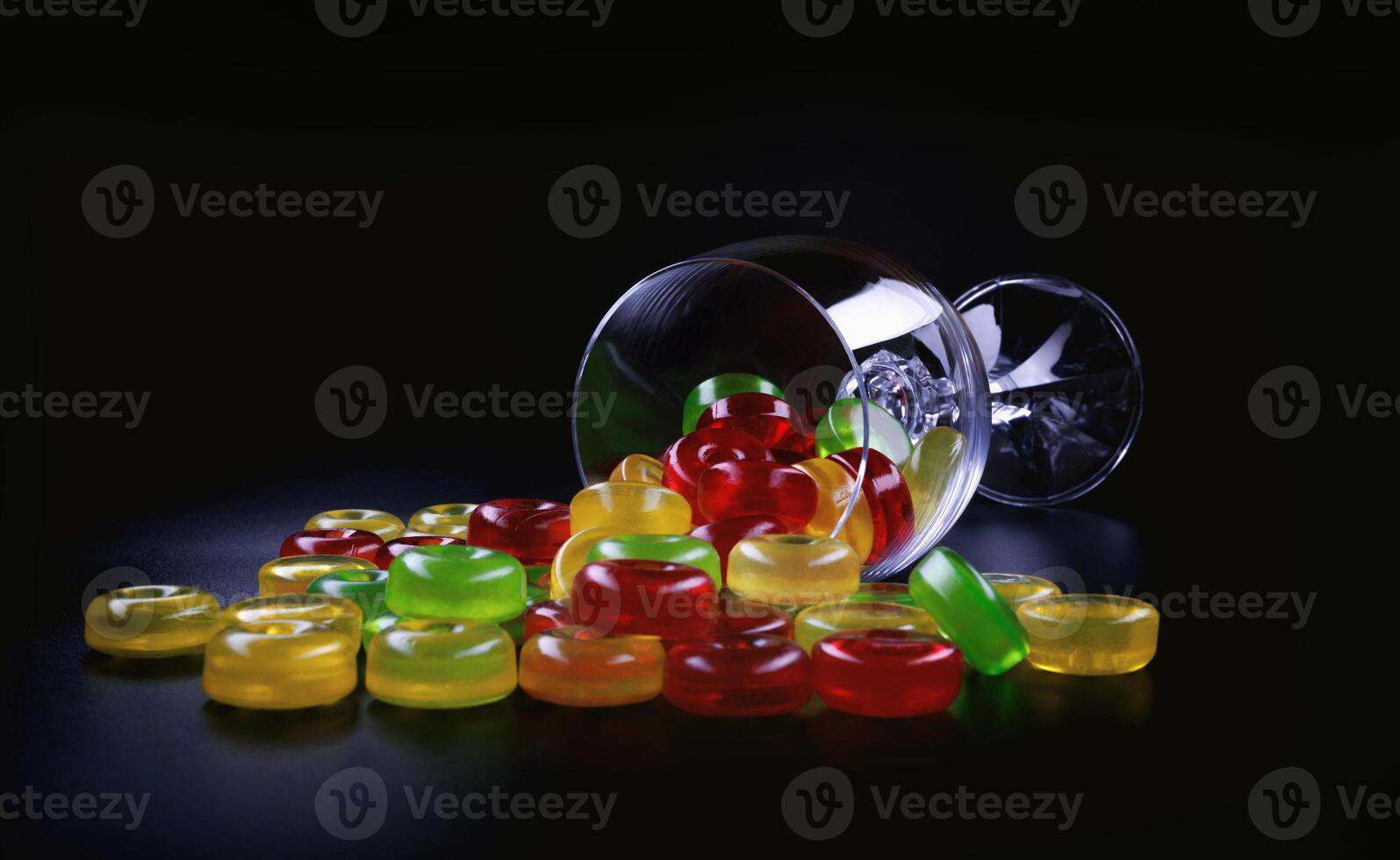 A lot of lollipops are scattered from an overturned glass goblet. Multi-colored candies in a glass. photo