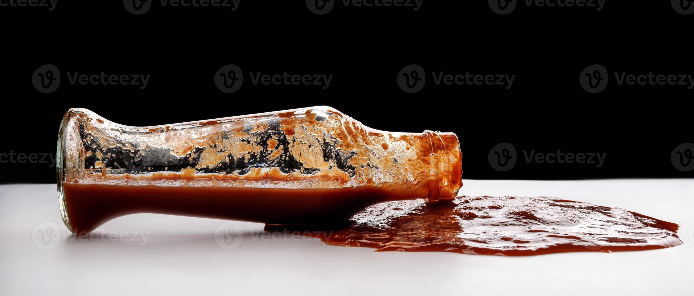 Tomato sauce . A glass bottle with ketchup and a puddle of ketchup spilled around it. photo