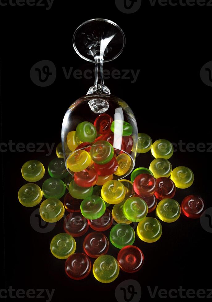 Many lollipops spill out from an overturned glass goblet. Multi-colored candies in a glass on a black background. photo