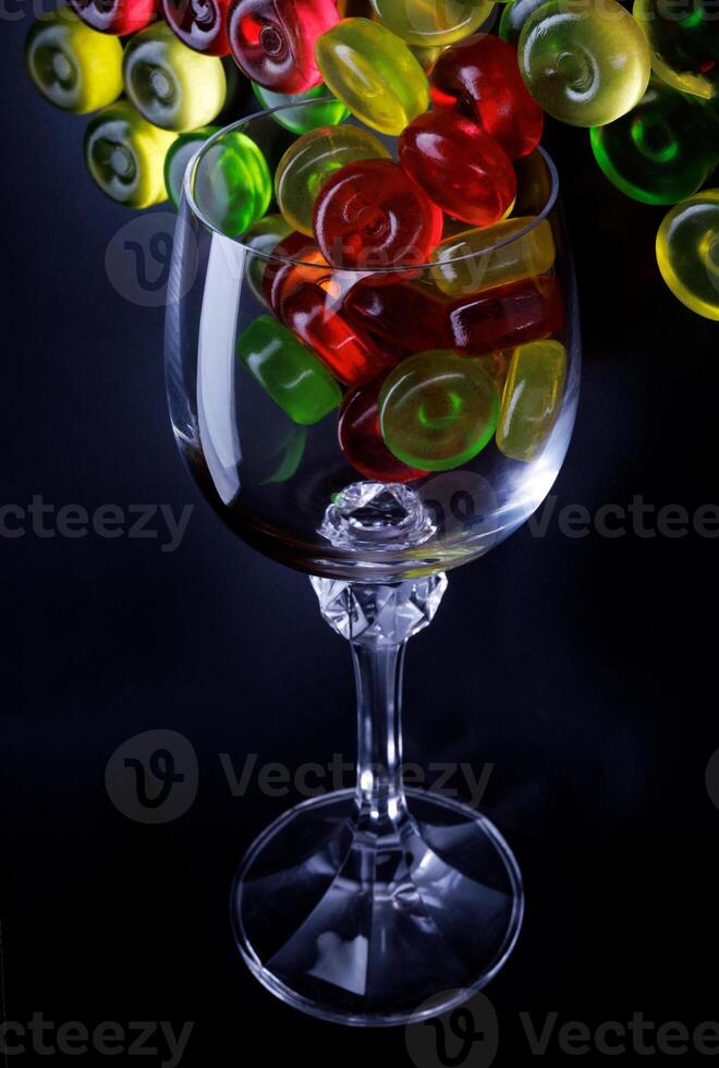 Many lollipops spill out from an overturned glass goblet. Multi-colored candies in a glass on a black background. photo