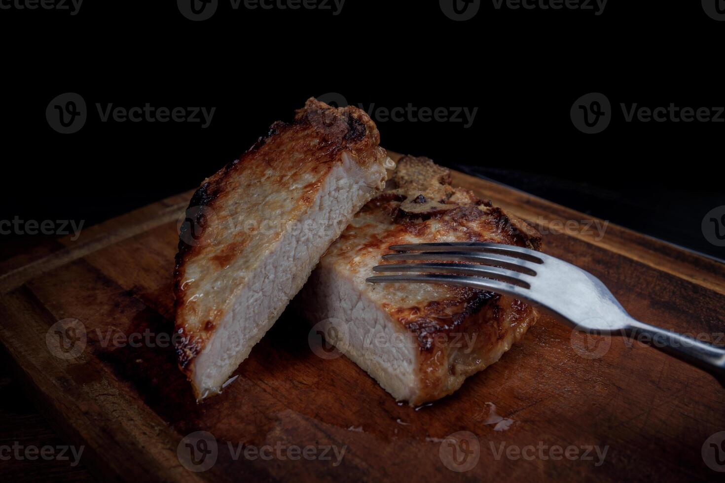 Roasted pork entrecote cut into pieces on a wooden cutting board. Fork in meat. photo