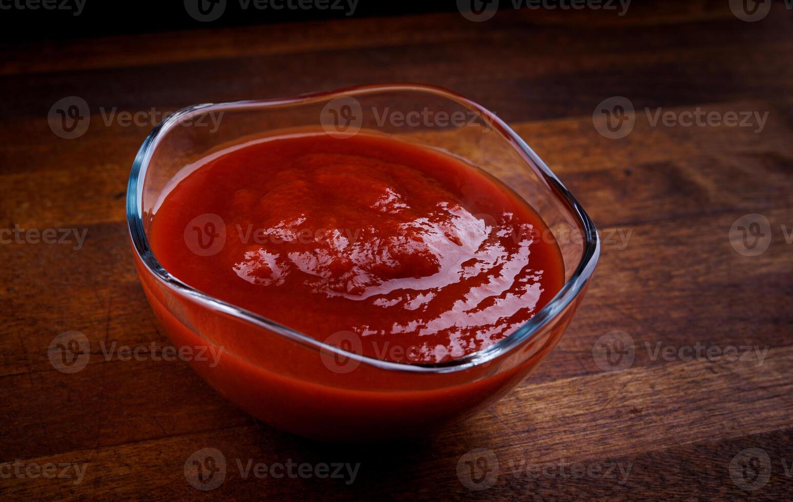 Ketchup in a glass cup on a wooden board. photo