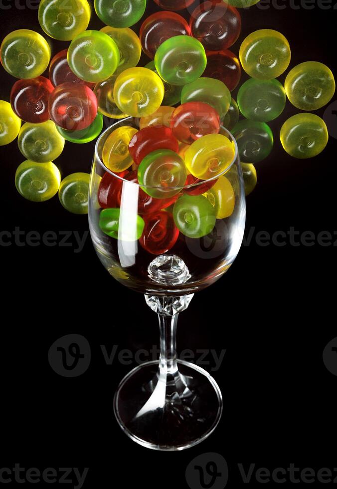 Many lollipops spill out from an overturned glass goblet. Multi-colored candies in a glass on a black background. photo