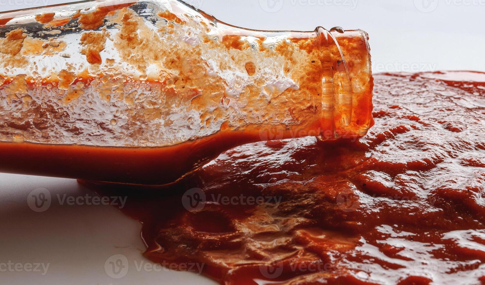 Tomato sauce . A glass bottle with ketchup and a puddle of ketchup spilled around it. photo