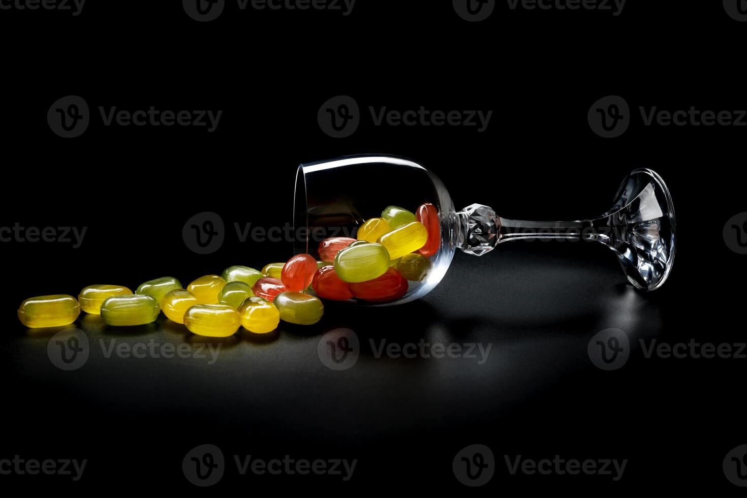 A lot of candy canes are scattered from an overturned glass goblet. Multi-colored candies in a glass on a black background. Marmalade candies. photo