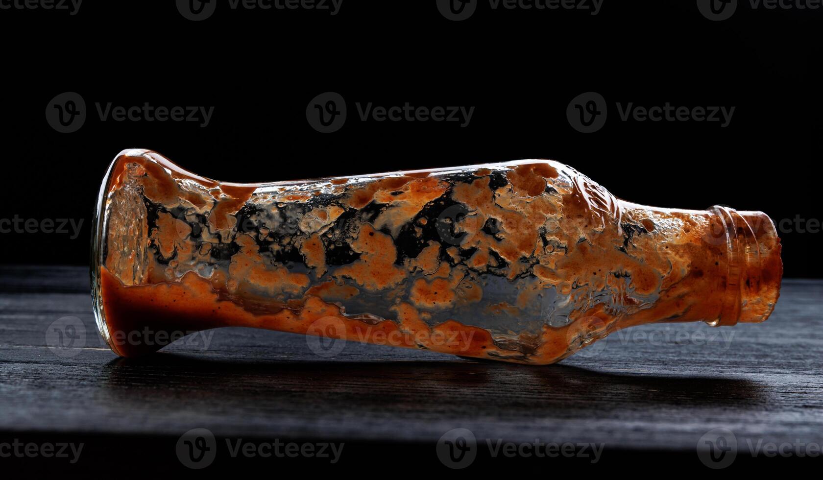 Tomato sauce . Empty ketchup bottle. Glass bottle with remaining ketchup inside on a black background. photo
