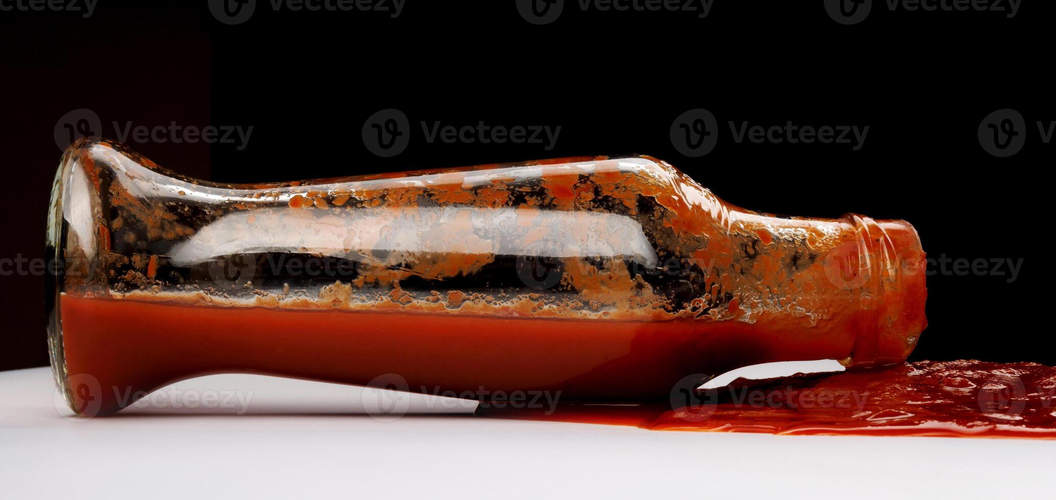 Tomato sauce . A glass bottle with ketchup and a puddle of ketchup spilled around it. photo