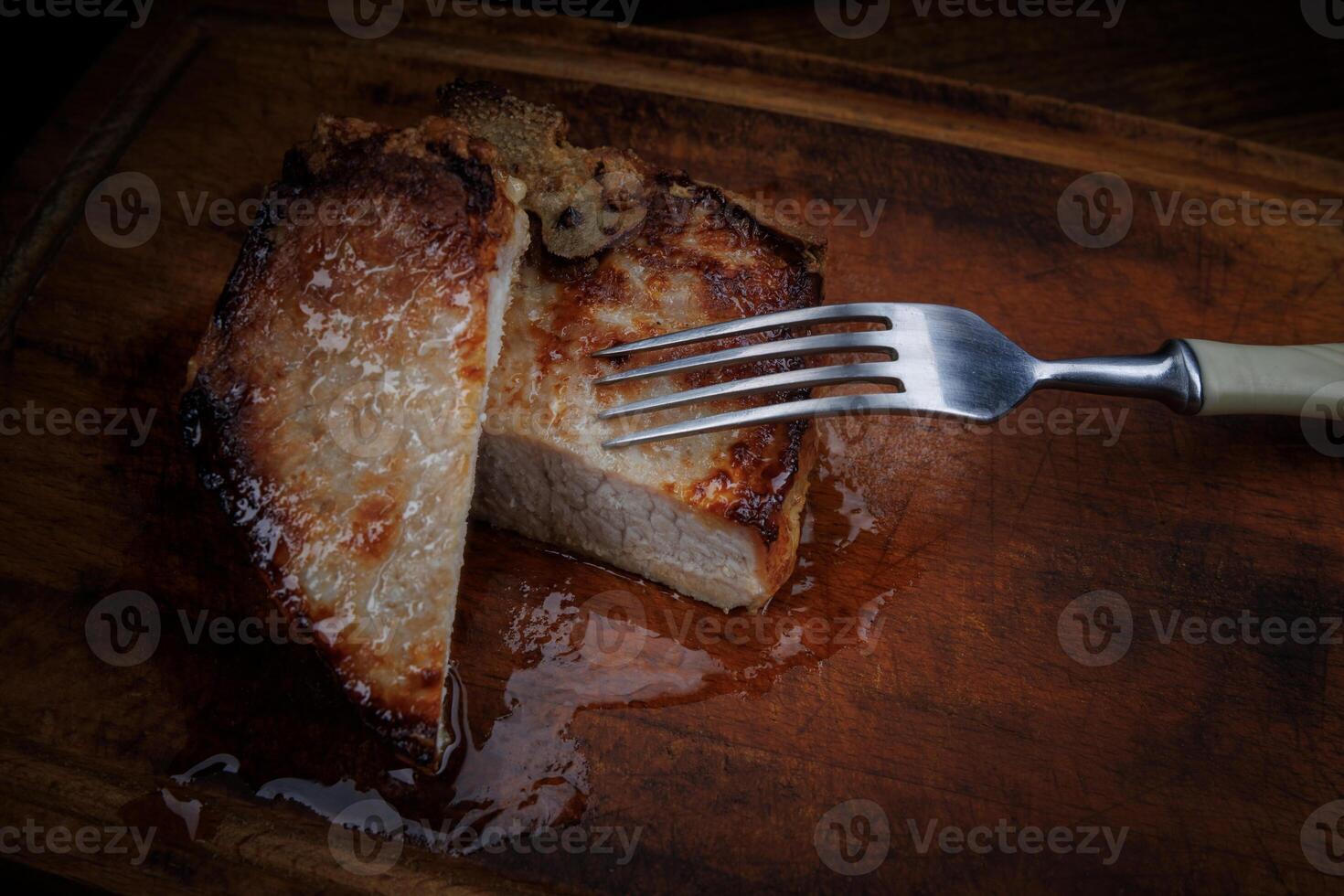 Roasted pork entrecote cut into pieces on a wooden cutting board. Fork in meat. photo