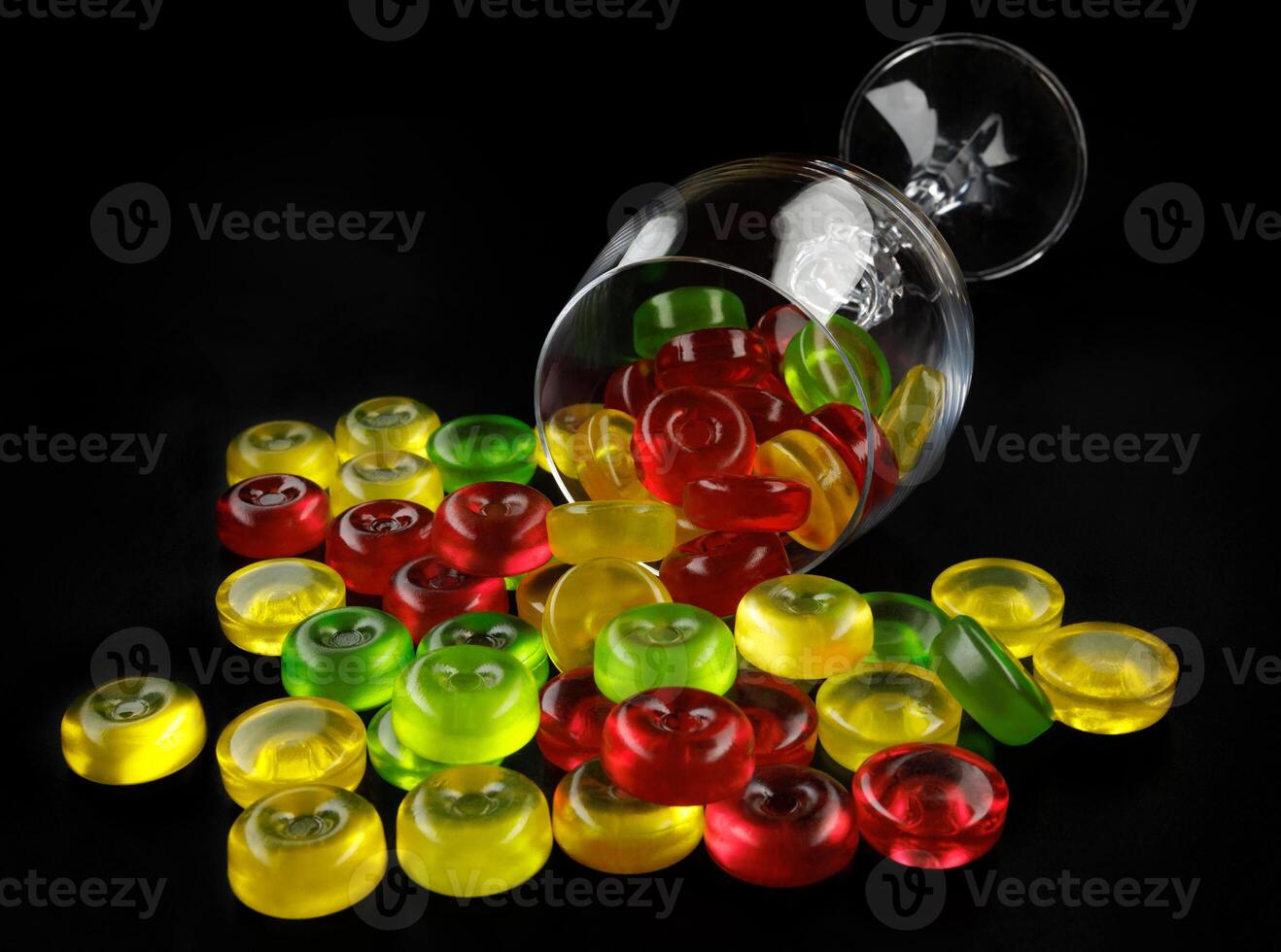 A lot of lollipops are scattered from an overturned glass goblet. Multi-colored candies in a glass. photo