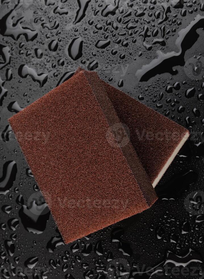 Melamine sponge on a black wet background. Beautiful drops of water around a melamine sponge. photo