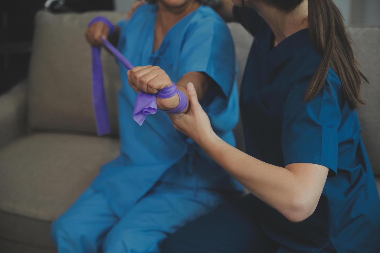 Personal trainer assisting senior woman with resistance band. Rehabilitation physiotherapy worker helping old patient at nursing home. Old woman with stretch band being coached by physiotherapist. photo