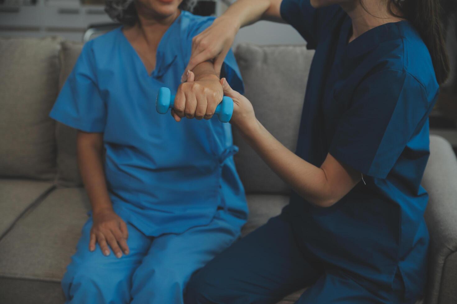 Old woman training with physiotherapist using dumbbells at home. Therapist assisting senior woman with exercises in nursing home. Elderly patient using dumbbells with outstretched arms. photo