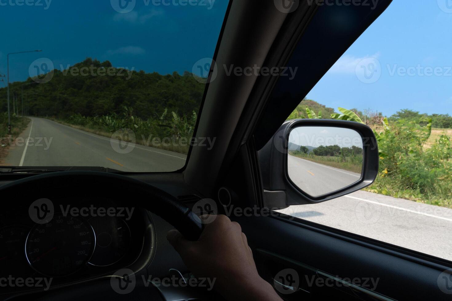 View from the inside of a car. View from the driver's seat. Driving on the asphalt road with nature of tree and mountain beside road. Under blue sky in the day time. photo