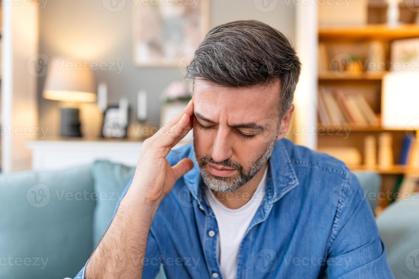Closeup of man suffering from headache at home, touching his temples, copy space, blurred background. Migraine, headache, stress, tension problem, hangover concept photo