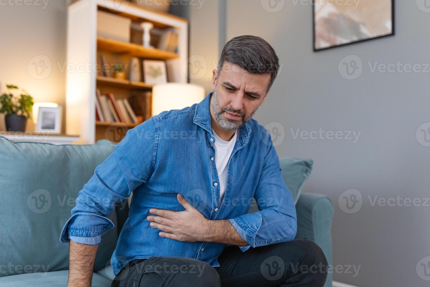Terrible stomachache. Frustrated handsome young man hugging his belly and keeping eyes closed while lying on the couch at home photo