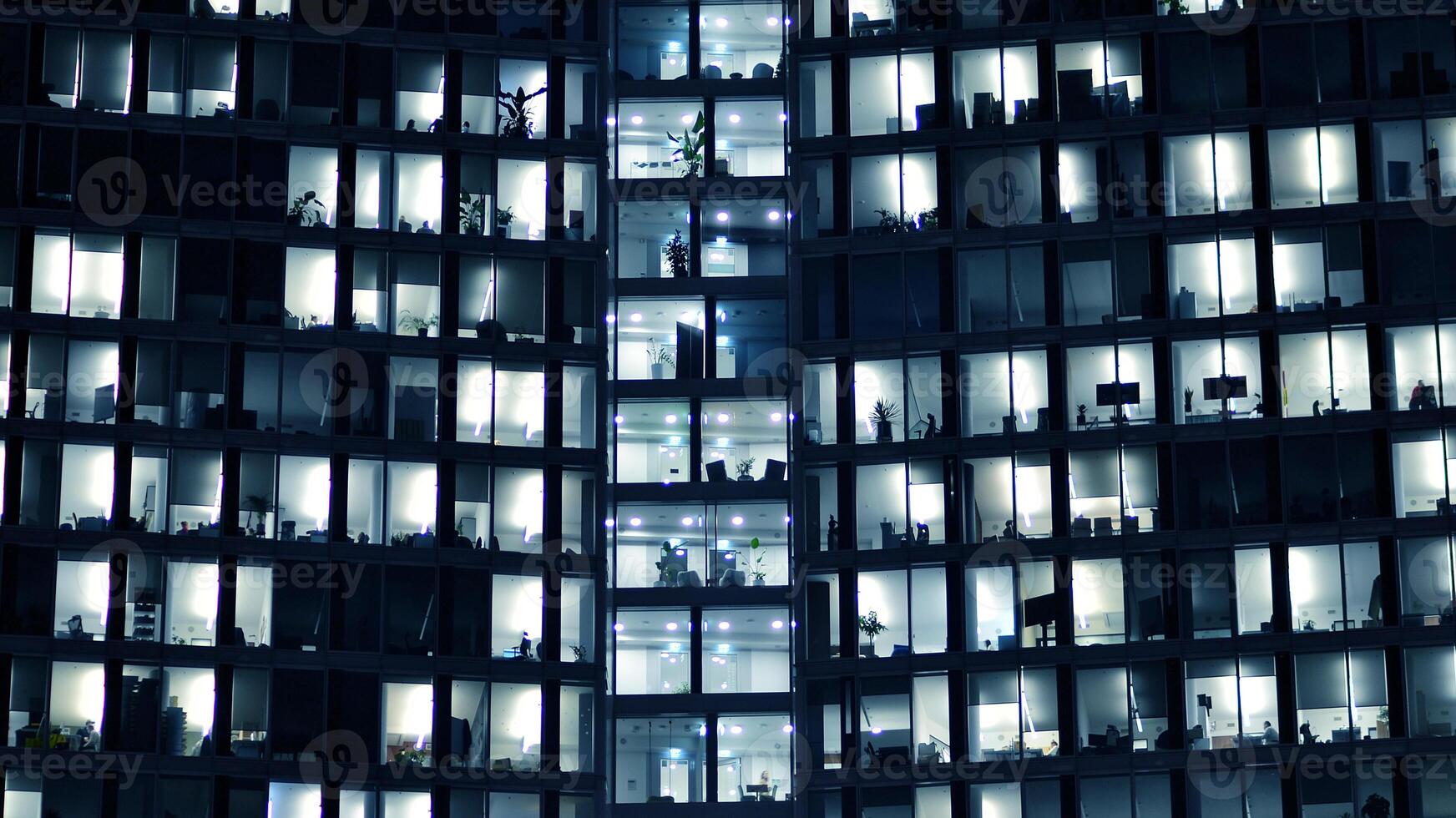 Fragment of the glass facade of a modern corporate building at night. Modern glass office in city. Big glowing windows in modern office buildings at night, in rows of windows light shines. photo