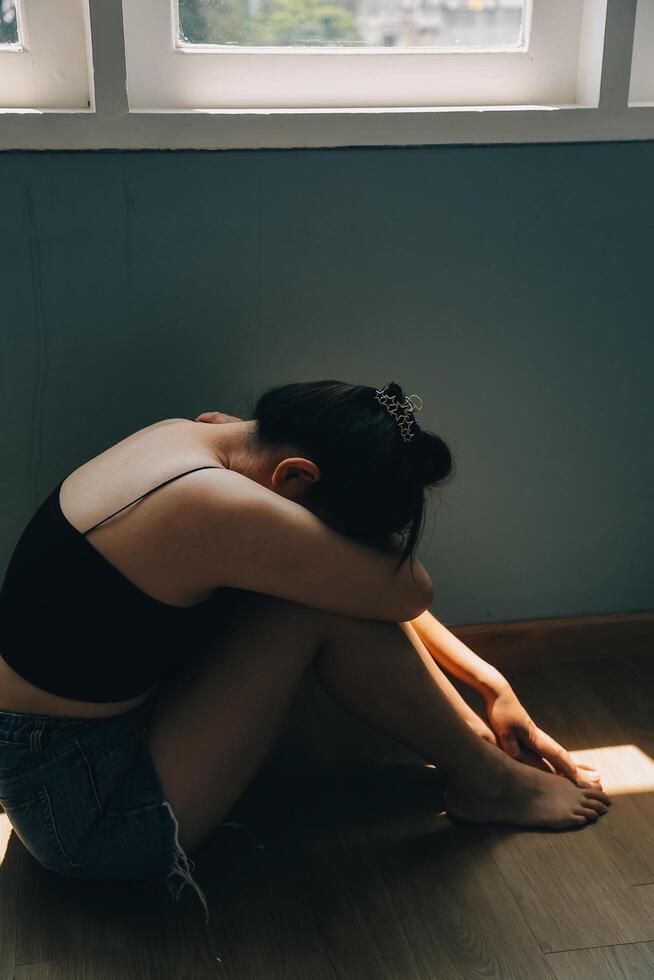 Thoughtful girl sitting on sill embracing knees looking at window, sad depressed teenager spending time alone at home, young upset pensive woman feeling lonely or frustrated thinking about problems photo