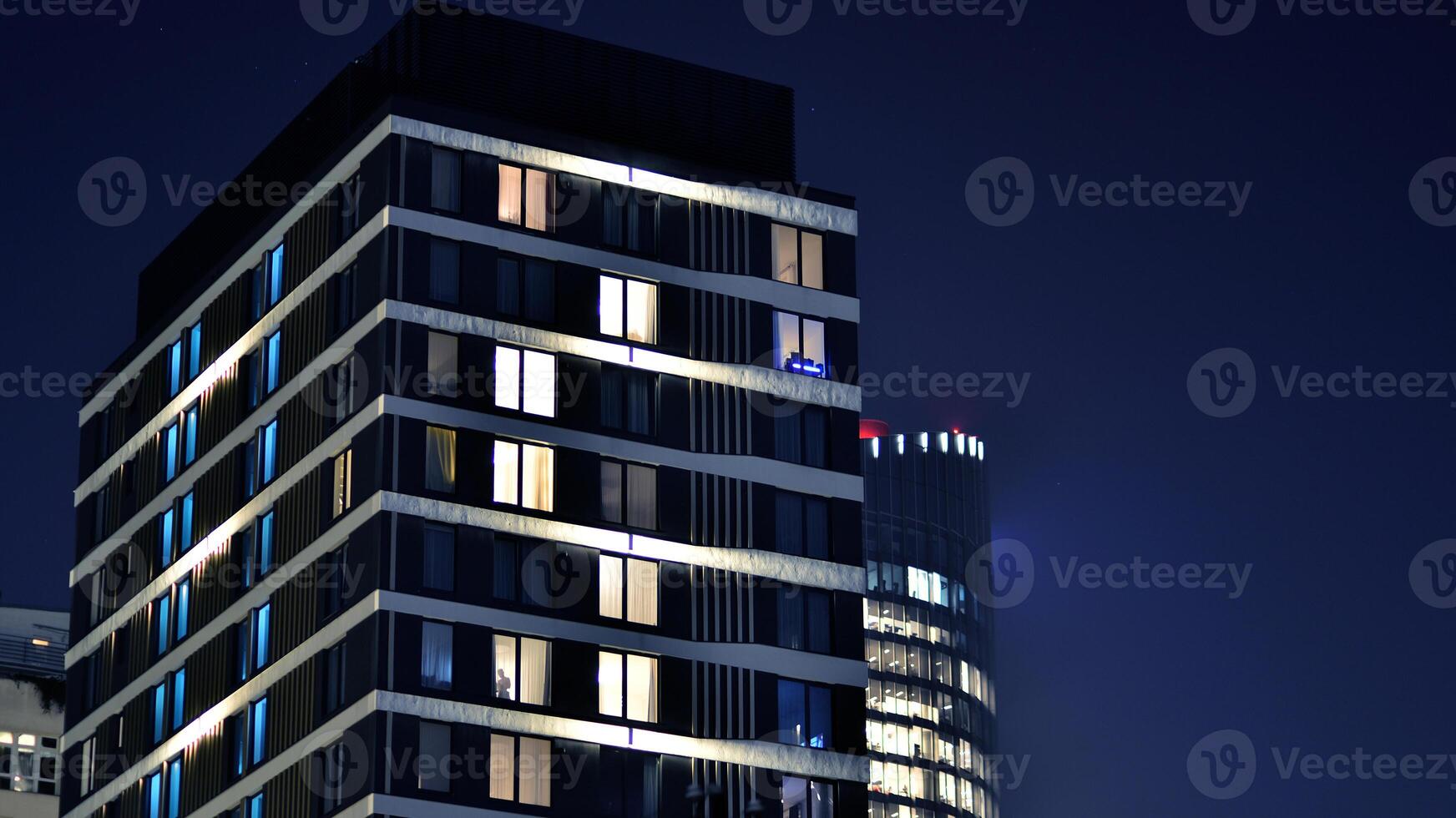 Glowing windows of the multi-storey building in night. View of modern residential building in downtown. photo