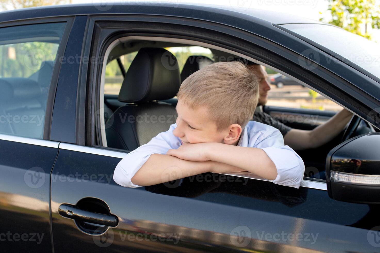 The cute boy climbed out of the car window and looks away. Go with Dad in the car photo