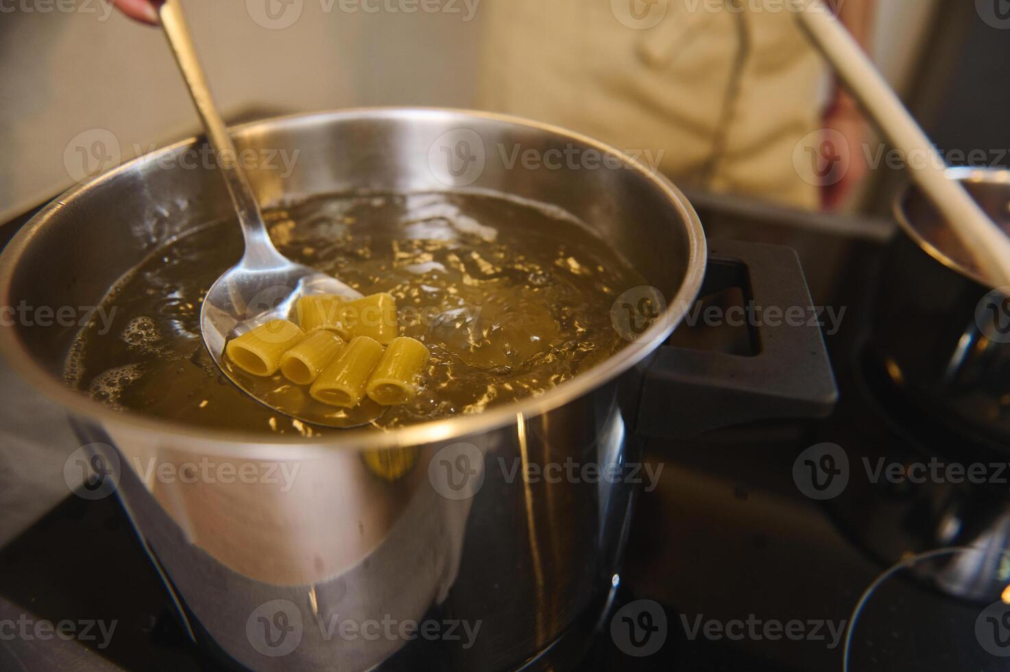 Close-up mixing Italian pasta in a boiling water, preparing spaghetti to the condition Al Dente. Chef cooking pasta, standing at electric stove or induction cooker. Extreme closeup photo
