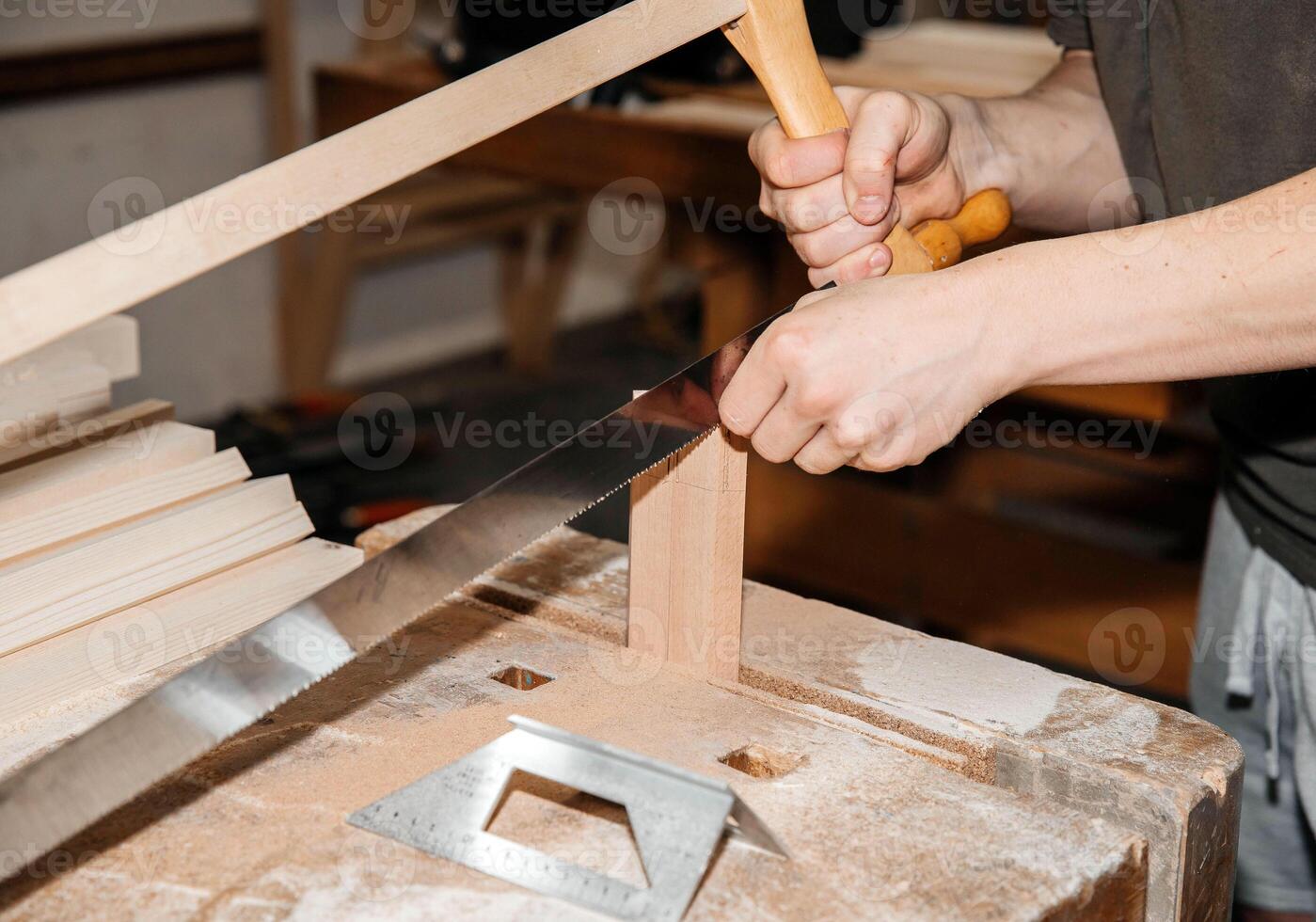 Hands cutting wood with saw on a dusty workshop table photo