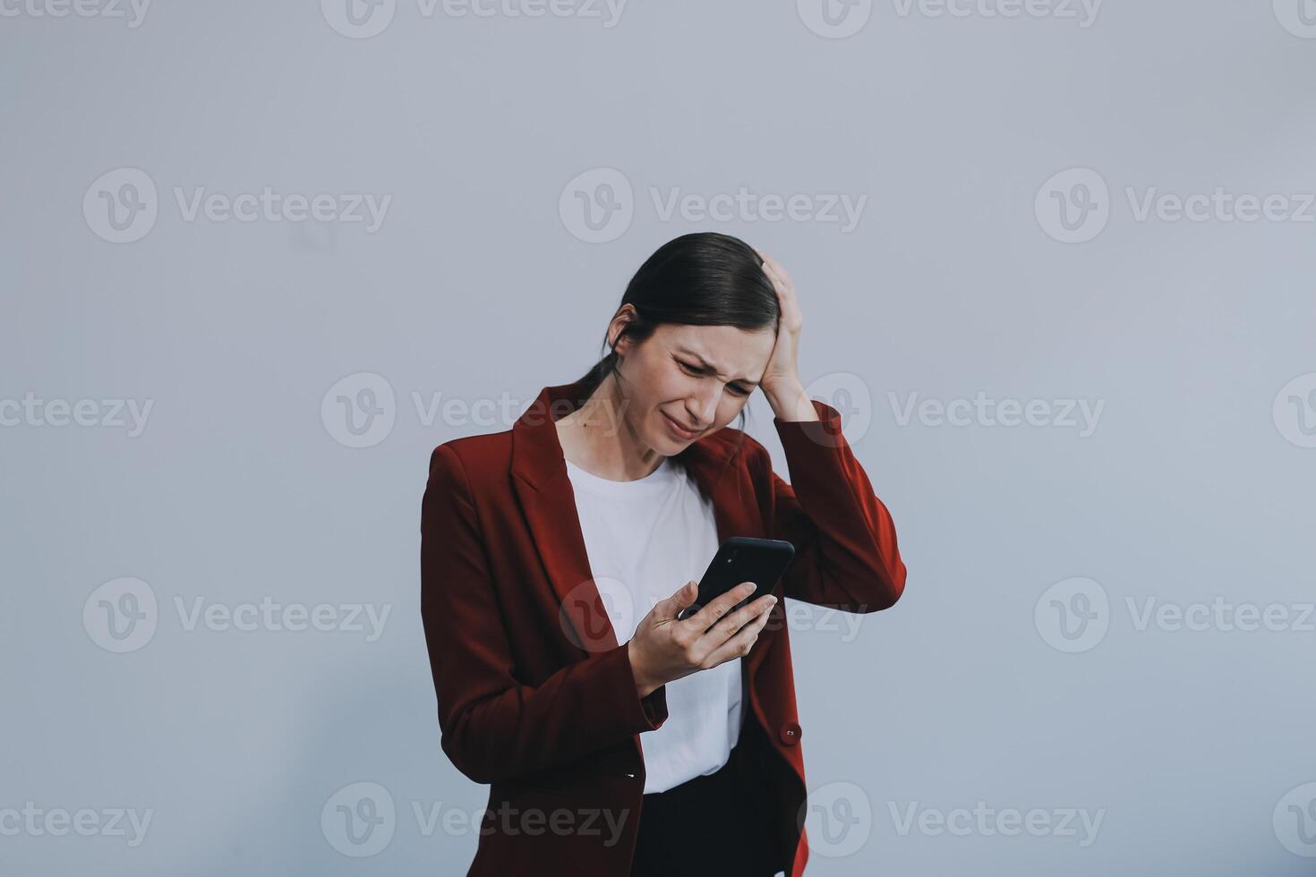 Annoyed angry young woman mad about spam message stuck phone looking at smartphone isolated on blank studio background, furious teen girl having problem with cellphone irritated by broken mobile photo