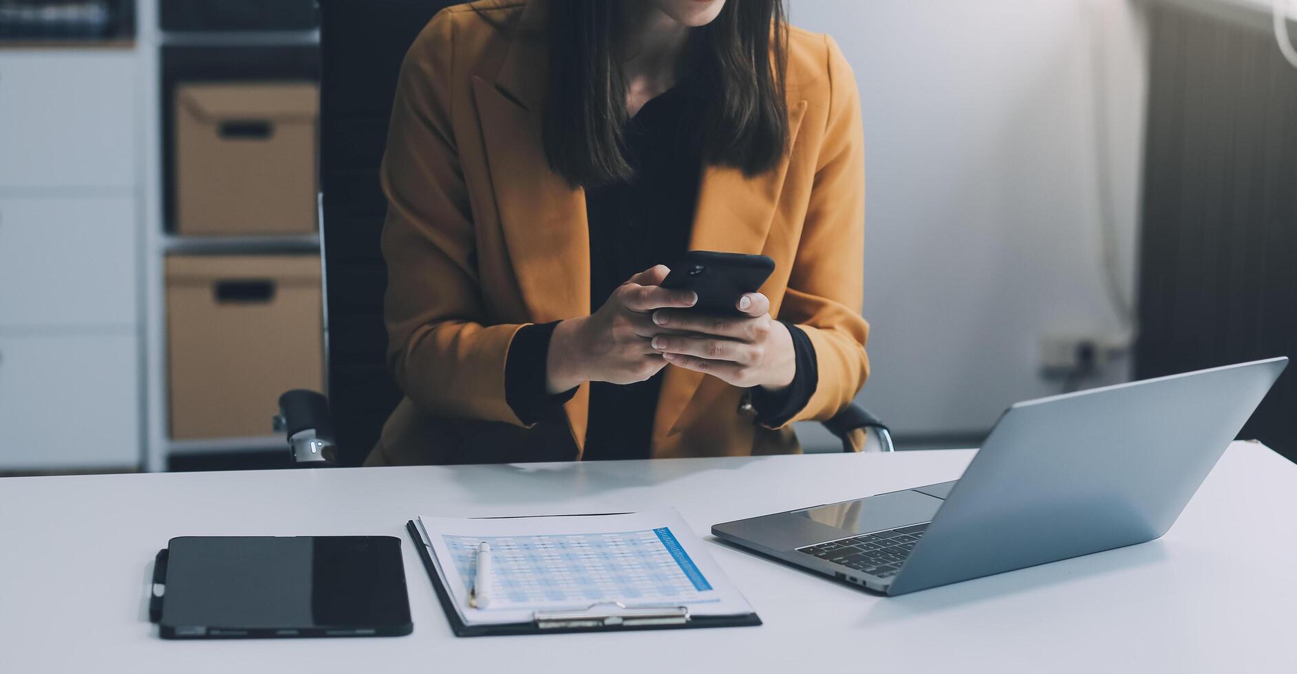 Beautiful Asian woman using a smartphone and working with a laptop while sitting at an office desk, working from home concept. photo