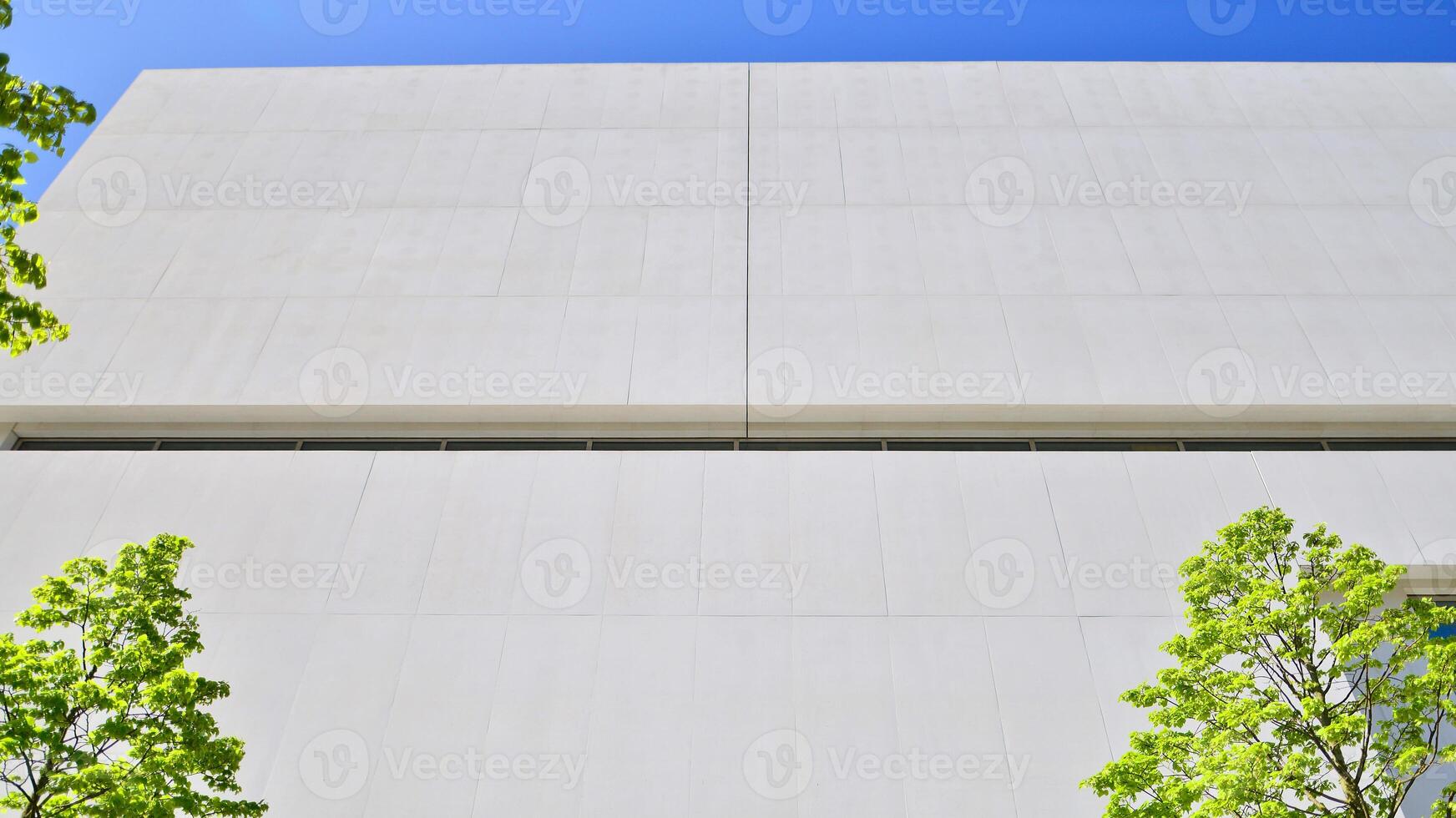 Modern white concrete building walls against blue sky. Eco architecture. Green trees and concrete office building. The harmony of nature and modernity. photo