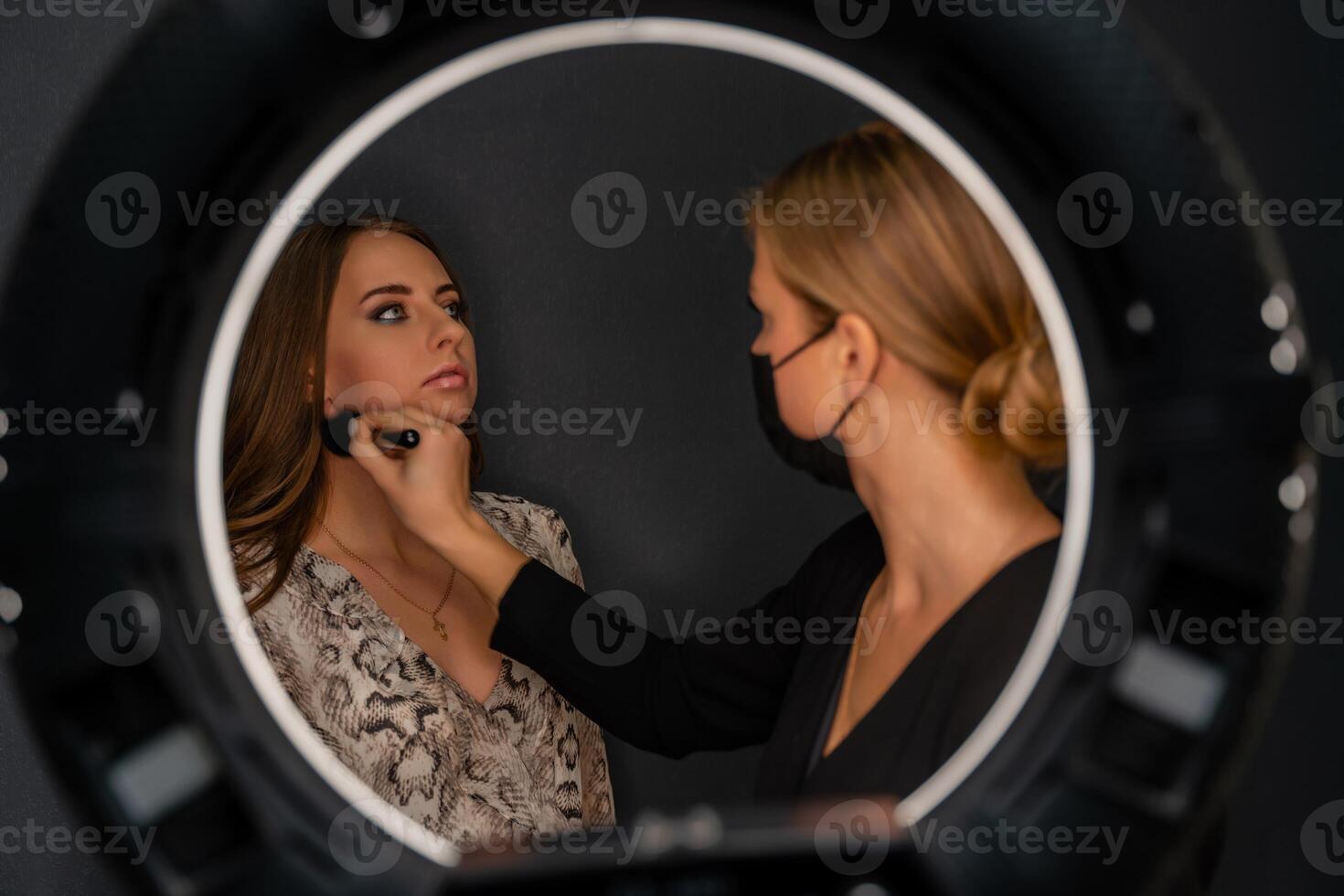 Makeup beauty salon. Makeup artist applies powder and blush. Beautiful female face. Makeup master's hand puts blush on cheeks of beauty model girl. Makeup in progress photo