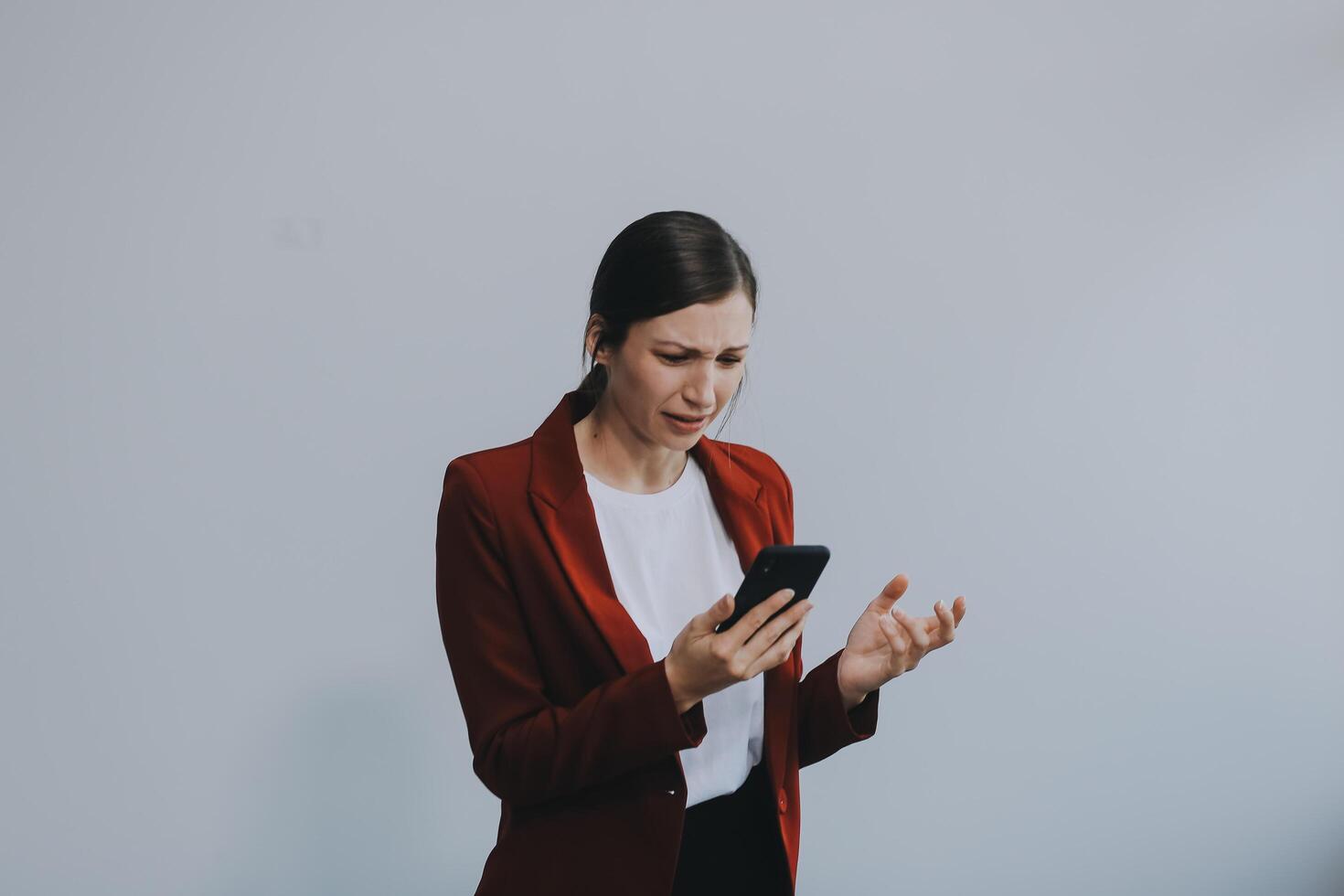 Annoyed angry young woman mad about spam message stuck phone looking at smartphone isolated on blank studio background, furious teen girl having problem with cellphone irritated by broken mobile photo